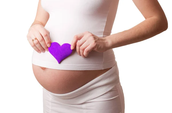 Pregnant woman put a violet toy heart to his stomach isolated on white — Stock Photo, Image
