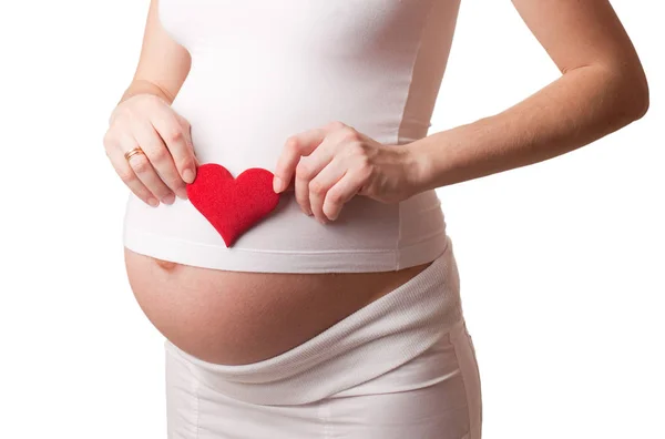 Pregnant woman put a red toy heart to his stomach isolated on white — Stock Photo, Image