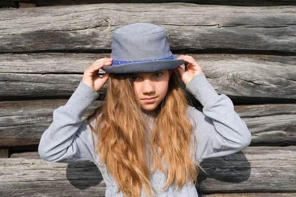 Радостная девочка-подросток с длинными волосами в повседневной одежде и синей шляпой, позирующей у деревянной стены. Активный образ жизни. Мода молодежи — стоковое фото