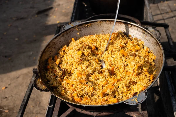 Sabroso pilaf uzbeko en un caldero en llamas al aire libre en stree —  Fotos de Stock