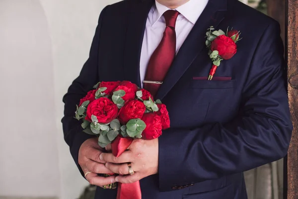 Röda rosor bröllop bukett i händerna på grrom — Stockfoto