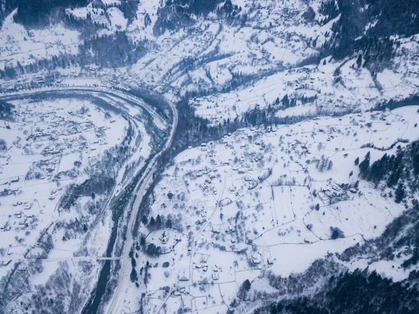 Calma y acogedor pueblo de cuento de hadas Kryvorivnia cubierto de nieve en las montañas Cárpatos, vista aérea. Paisaje típico en el Parque Nacional Hutsulshchyna en Ucrania. Vacaciones y deportes de invierno . Imagen De Stock