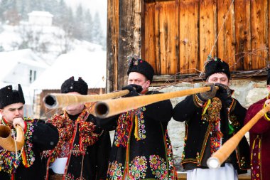 Hutzulian Koliadnyky ulusal Hutsul kostümü içinde Noel şarkıları söylüyor ve geleneksel trembita boynuzuyla çalıyor, Karpatya köyü Kryvorivnia