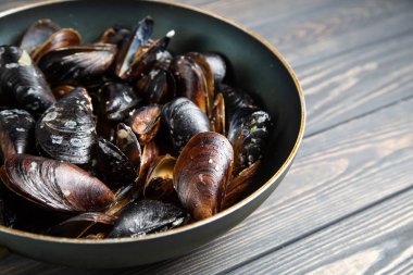 Maydanozlu midye ve ahşap masadaki tavada sarımsak.