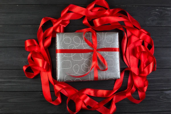 Grey silver gift box with red ribbon bow on black wooden table