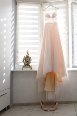 Bir askı bir pencere yakınında asılı parlak bej renkli gelinlik