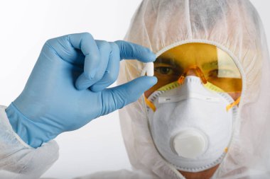 Tek kullanımlık anti-salgın takım elbiseli doktor koruyucu bir solunum cihazı takıyor ve gözlük beyaz arka planda tablet tutuyor.