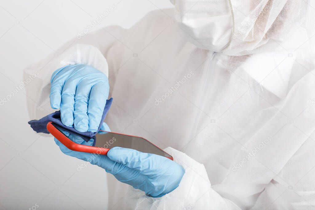 Hands in protective gloves and siut cleaning phone from dust and infection on white background