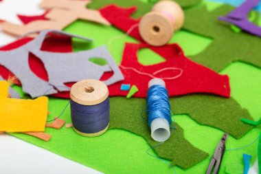 Beyaz masada renkli keçe, iplik, iğne ve makas.