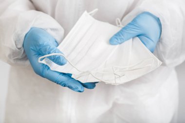 Beyaz arka plandaki enfeksiyondan korunmak için doktor elini tıbbi bir yüz maskesi ile kapat.