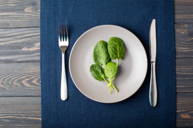 Mavi keten masa örtüsünün üzerindeki gri tabakta taze ıspanak yaprakları.