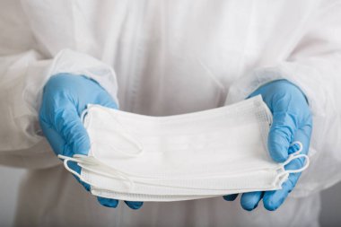 Beyaz arka plandaki enfeksiyondan korunmak için doktor elini tıbbi bir yüz maskesi ile kapat.