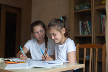 Masadaki genç kızlar ellerinde kitap ve defterlerle....