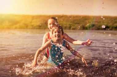 Zenci mayo giymiş küçük kızlar köydeki nehirde su sıçratıyorlar.