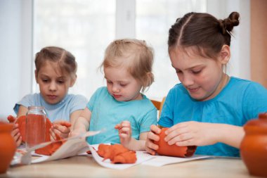Farklı yaşlarda üç kız kilden tabak yontuyorlar.