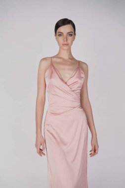 Zarif, şık elbiseli bir kadın. Stüdyoda pembe gece kıyafetleri içinde güzel bir model. Klasik ipek elbise. Seksi bayan beyaz arka planda kalsın. Klasik saç stili ve makyajlı mükemmel bir genç kadın.. 