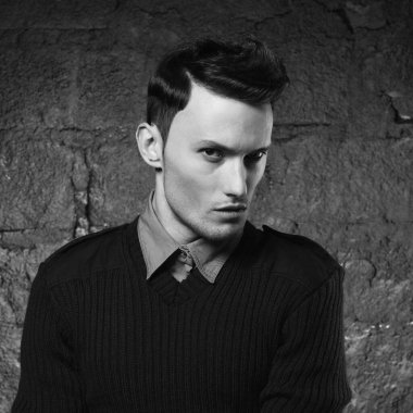 Duvara dayanmış yakışıklı ve şık bir adamın portresi. Genç bir adamın moda portresi. Modern saç stili olan çocuk..