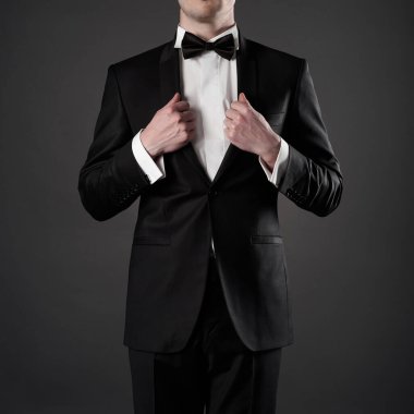 Zarif siyah takım elbiseli, kravatlı şık bir adamın fotoğrafı. Fotoğraf stüdyosunda modaya uygun genç bir poz. Beyaz gömlekle sigara içilen lüks bir akşam..