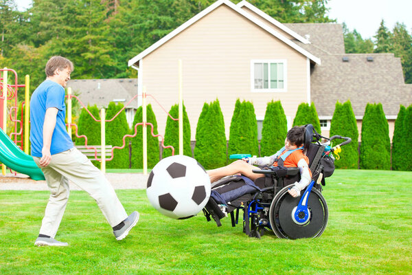  Father playing soccer with ten year old biracial disabled son in wheelchair