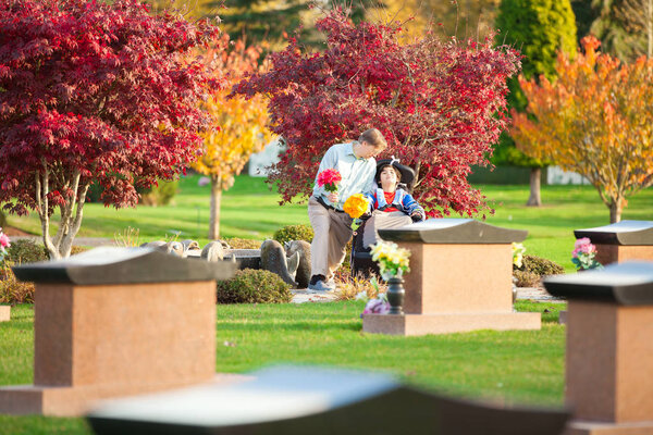 Father and disabled son in wheelchair  visiting gravesite in cem