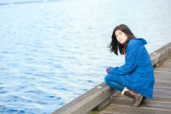 Sad, lonely biracial  teen girl on wooden pier by water — Stock Photo, Image