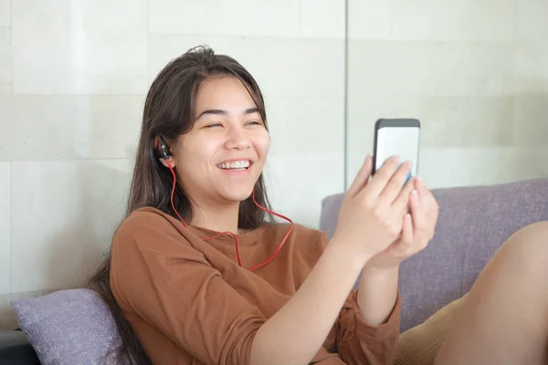 Biracial teen girl sitting on couch with smartphone, laughing — Stock Photo, Image