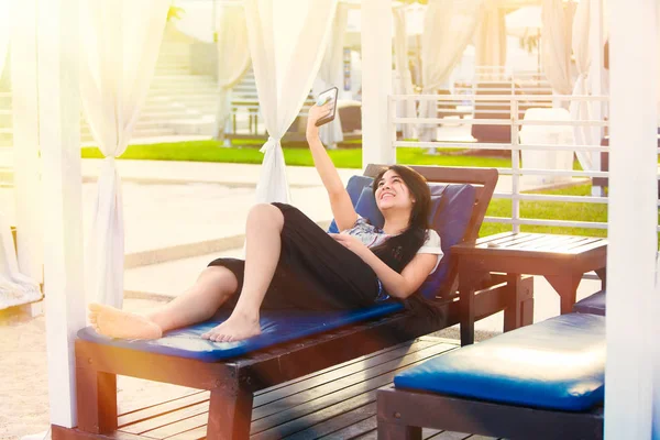 Biracial teen girl relaxing under sun shade using cellphone — Stock Photo, Image