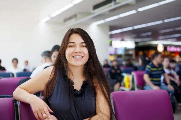 Chica adolescente sentada en la sala de salida del aeropuerto, sonriendo — Foto de Stock