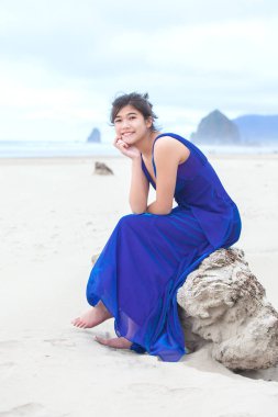 Sahilde oturan mavi elbiseli biracial genç kız