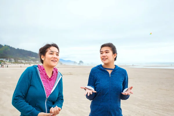 Две девочки-подростки гуляют по пляжу в прохладный облачный день — стоковое фото