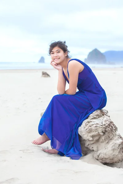 Biracial teen dívka v modrých šatech sedí na pláži — Stock fotografie