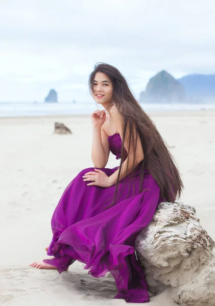 Biracial tiener meisje in paarse magenta jurk zittend op strand — Stockfoto