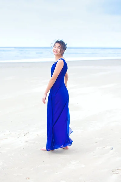 Adolescente vistiendo vestido azul en la playa mirando hacia atrás sobre el hombro —  Fotos de Stock