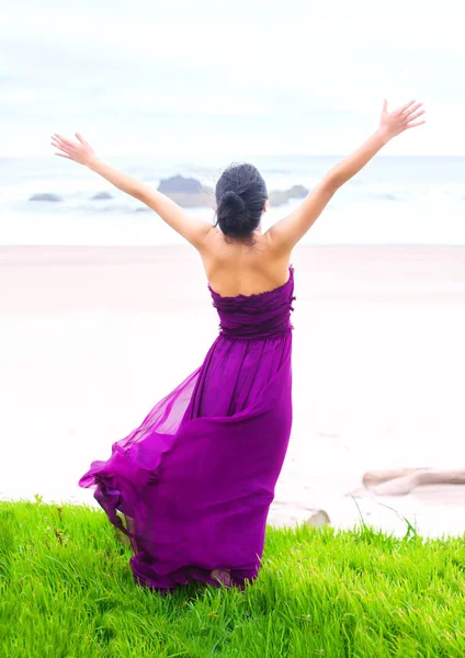 Tiener meisje dragen van paarse jurk armen verhoogd naar Oceaan — Stockfoto
