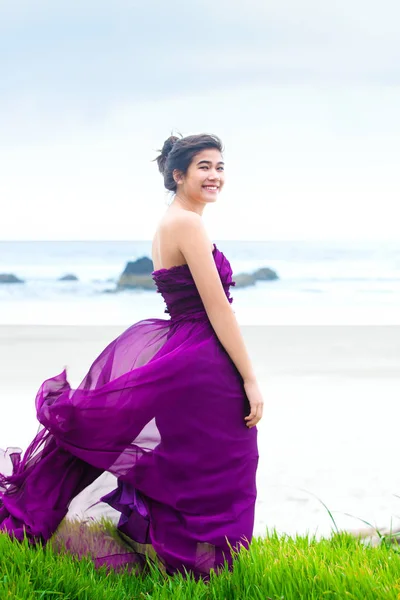 Adolescente chica vistiendo vestido púrpura en la hierba knoll con vistas al océano —  Fotos de Stock