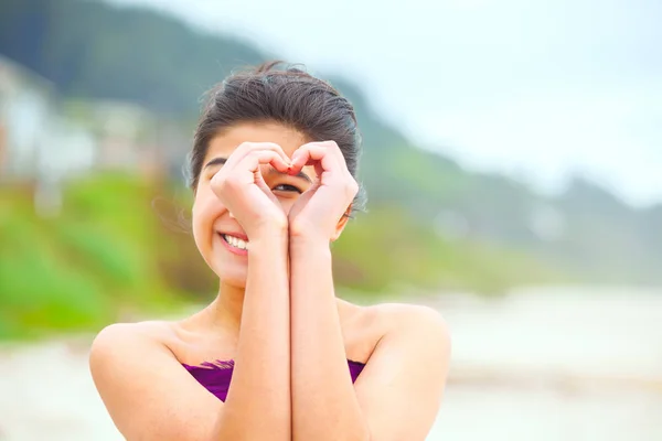 Fille sur la plage regardant à travers les mains en forme de coeur — Photo