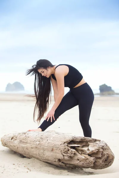 Ung kvinna stretching av loggen på stranden nära havet — Stockfoto