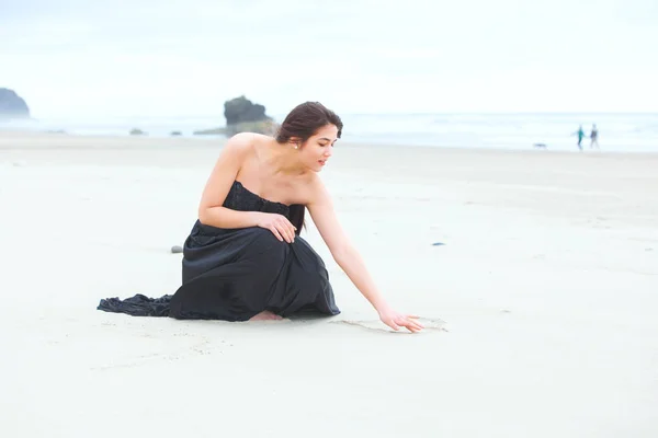 Diz çökmüş, kum plaj üzerinde yazma elbiseli genç kız — Stok fotoğraf