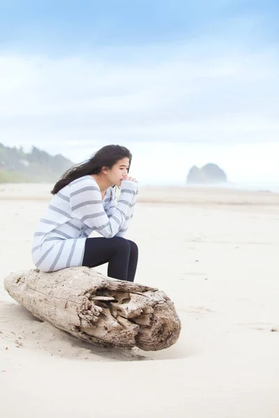Девушка-подросток сидит на бревне и спокойно смотрит на океан. — стоковое фото