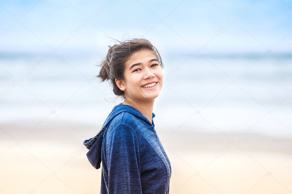 Happy, smiling teen girl in blue hoodie jacket  on beach