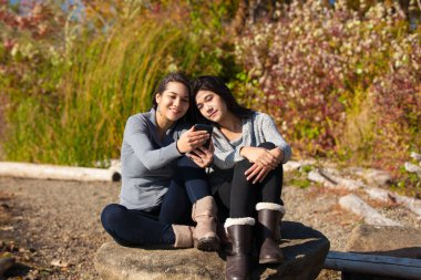 Smartphone göl kenarında sonbaharda kullanma kaya üzerinde genç kız