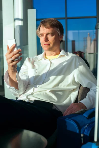 Tired businessman checking cellphone in airport terminal, restin — Stock Photo, Image