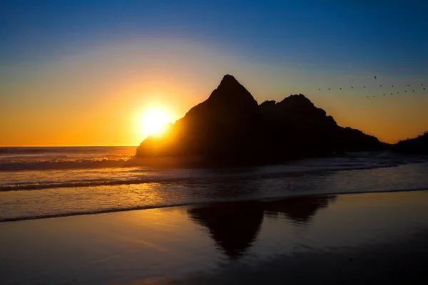 Soft beautiful sunset behind large rock along Pacific Ocean beac — Stock Photo, Image