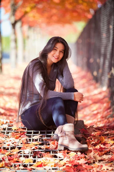 Teenie-Mädchen sitzt im Herbst unter bunten Ahornbäumen — Stockfoto