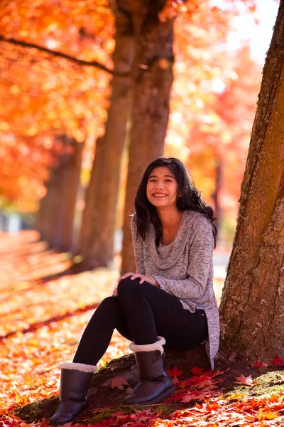 Biracial teen girl sitting under colorful maple trees in autumn — Stock Photo, Image