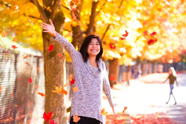 Tiener meisje gooien kleurrijke herfst bladeren in lucht onder de bomen — Stockfoto