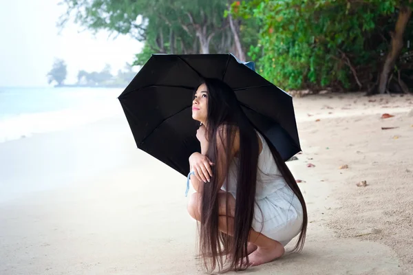 Молодая женщина на пляже держит зонтик, глядя вверх на дождь — стоковое фото