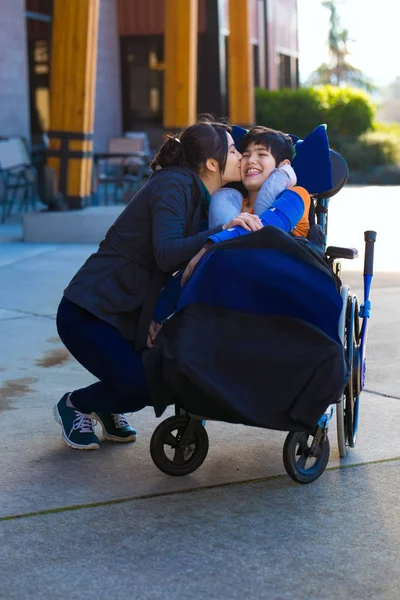 Hermana mayor besándose pequeño hermano discapacitado en silla de ruedas outdo — Foto de Stock