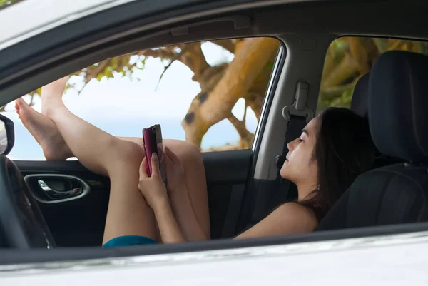 Дівчина-підліток за допомогою смартфона розслабляється з ногами на вікні автомобіля — стокове фото