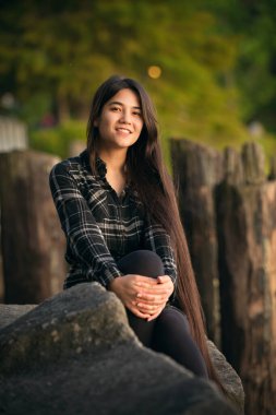 Smiling biracial young woman sitting on rocks outdoors at sunset